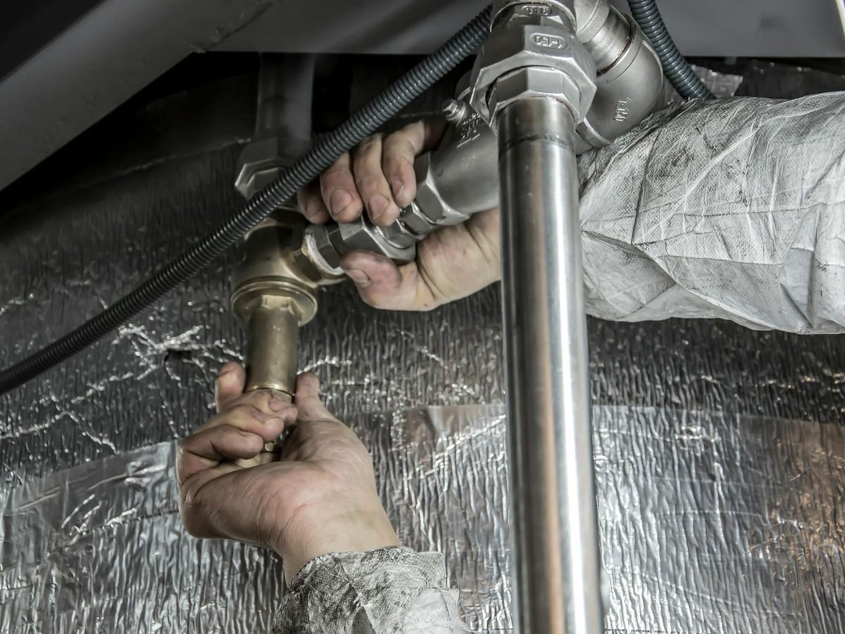 A plumber fitting metal pipework indoors with both hands visible